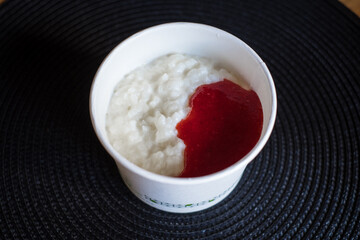 Rice flake porridge in a white round carton take-away box with fresh strawberry jam. Healthy breakfast bowl delivery food to-go.
