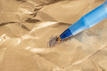 blue ball pen tip scribbling on golden paper texture.