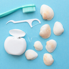 Tooth model with caries, toothbrush, dental floss and seashells. Blue background. Flat lay. Top view. Benefits of minerals for dental hygiene. Oral care. Square photo.