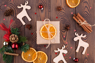 Fototapeta na wymiar Christmas holiday background with wooden deer, christmas tree decorated with pine cone, beads and gifts wrapped in craft paper, dried oranges on wooden background, flat lay, copy space.