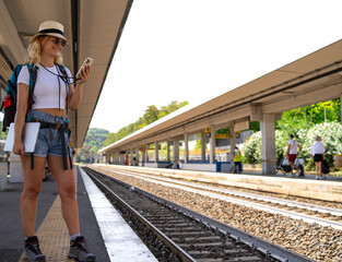 Woman waits for train at station while working happily on phone, digital nomad, travel and...