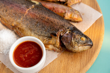 Large and small fried fish on a wooden board, Sauce, salt. close-up.