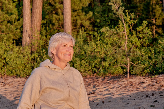 Senior white smiling woman on background of forest, illuminated by sun on sunset.