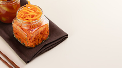 Probiotic food. Pickled or fermented vegetables. Korean carrot in glass jar on a brown napkin with chopsticks on a kitchen table with copy space. Home food preserving or canning. Close up