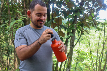 Sporty young man opening an orange bottle with a black cap closeup