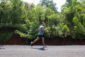 Young mid weight man jogging on the unpaved road with green background