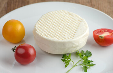 A head of brined cheese lies on a white plate with tomatoes and parsley. Selective focus.