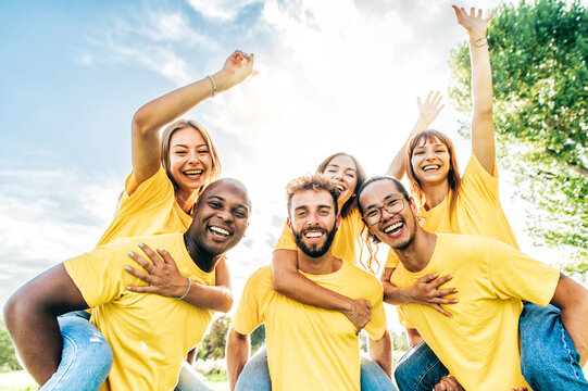 Multiracial smiling friends dressed in yellow doing the piggy back - Lifestyle concept of volunteers doing great teamwork - Group of happy young people having fun together