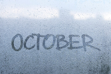 Finger drawing on the misted glass. Autumn rainy weather. The inscription on the window: October