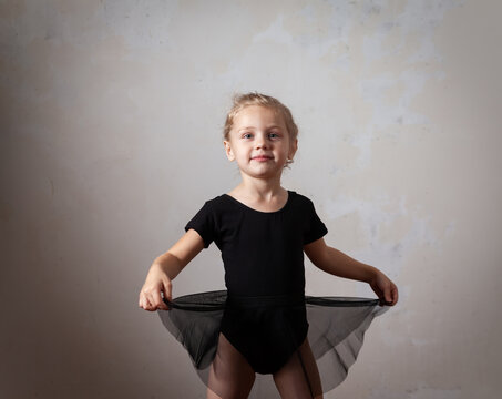  little girl in   black swimsuit performs   ballet  exercise on  light background