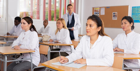 Fototapeta premium International group of different age people in white coats sitting in lecture hall at refresher course
