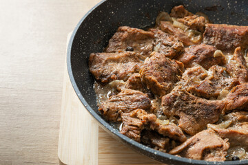 Fried beef with onions and spices in a frying pan on a light texture background. Meat recipe. Juicy grilled steak, close-up. Place for text, space for copy.