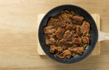 Fried beef with onions and spices in a frying pan on a light texture background. Meat recipe. Juicy grilled steak, close-up. Place for text, space for copy.