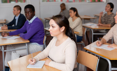 Portrait of focused young woman on lesson in school auditorium. Adult learning and education concept