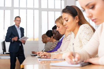 Focused young attractive Latina listening to lecture in classroom with group. Postgraduate...
