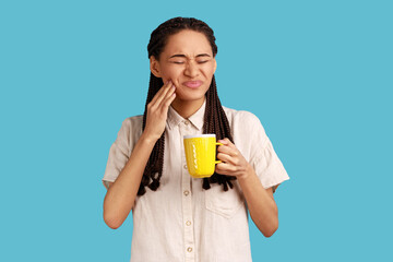 Portrait of unhealthy woman with black dreadlocks wearing white shirt. holding cup in hands, having...