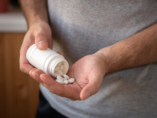 The man pours large white pills into the palm of his hand from a white plastic jar. Treatment and prevention of diseases