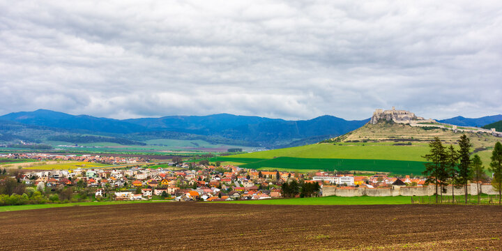 spisske podgradie, slovakia - APR 29, 2019: rural landscape on a cloudy day. trees along arable on the hill. village and the castle in the distance in front of a mountain ridge