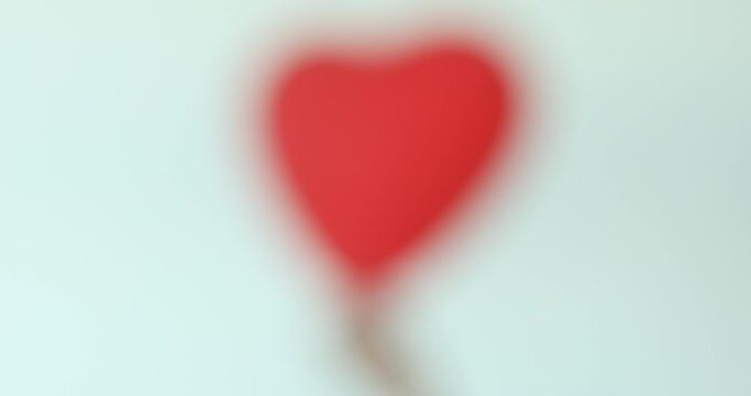 Moving image of blurred and slowly focused shaked red heart shape balloon in cropped woman hand. Valentines holidays