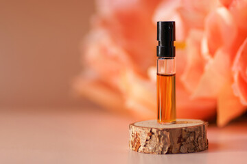 Perfume sample with orange liquid on woooden podium with peonies in soft focus as background. Pipette with fluid hyaluronic acid, serum, retinol. Natural cosmetics, health care, beauty mockup