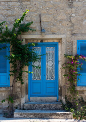 Fototapeta na wymiar View of old, historical, traditional stone house with blue colored door and windows in famous, touristic Aegean town called Alacati. It is a village of Cesme, Turkey. It is a sunny summer day