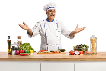 Cheerful mature male chef posing behing a kitchen counter with vegetables