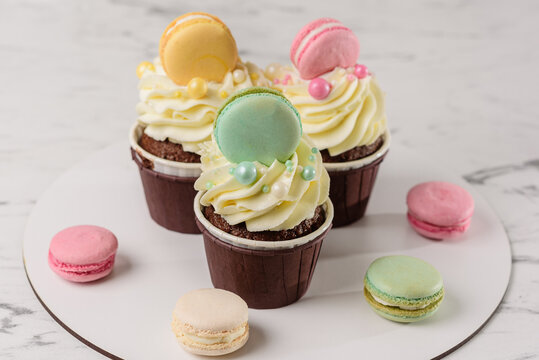 Sweet colorful macaroons with chocolate cupcakes on a white tray. Dessert concept as a gift, holiday desserts.
