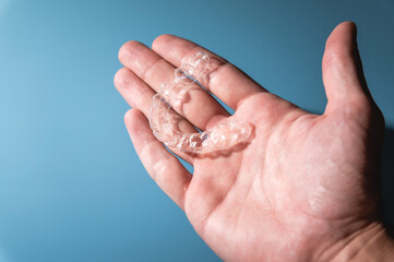 Close-up of a man holding invisible aligners for whitening and straightening his teeth on a blue background. Orthodontic treatment instead of or after braces
