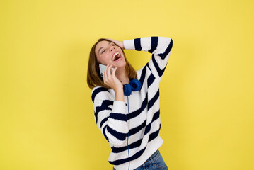 Portrait of cute happy teenage girl wearing talking on mobile phone and smiling  over yellow background. Copy space.