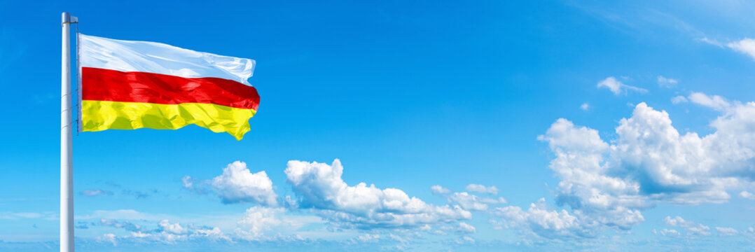 South Ossetia flag on a blue sky *** Horizontal banner 12000 x 4000 px