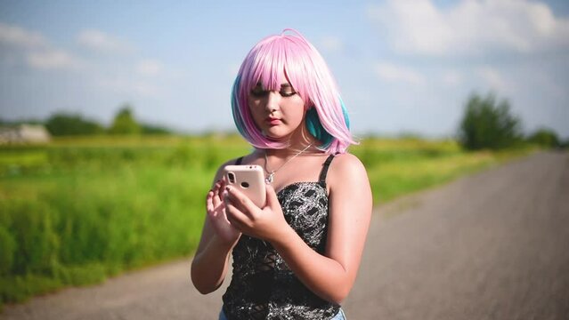 Cosplay, anime girl in pink wig typing telephone. Teenage girl uses smartphone outdoors.Horizontal video
