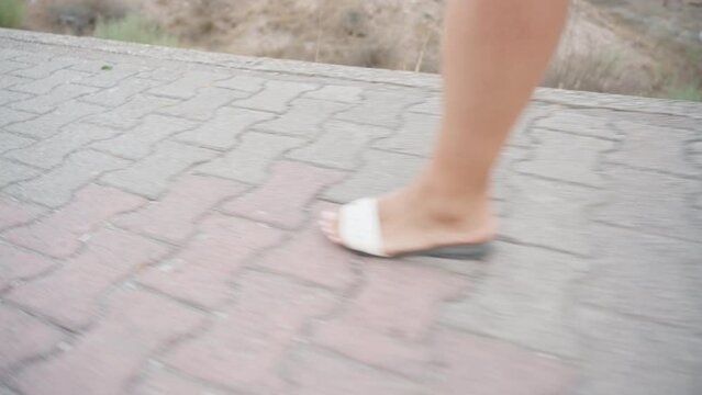 The girl's feet in sandals walk on the tile, the camera rotates.