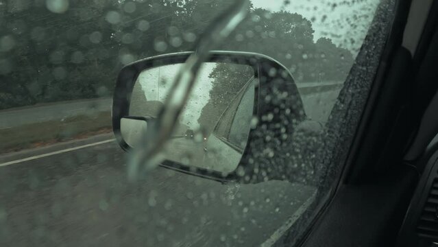 Side drivers car mirror with rain droplets. Driving automobile while rainy weather, busy road