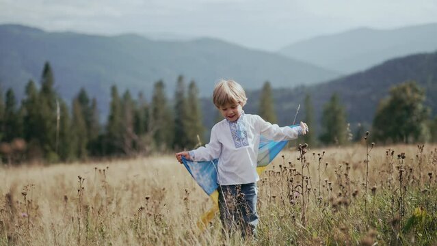 Lovely little boy - Ukrainian patriot child with national flag on meadow of Carpathian mountain, open area. Ukraine, peace, independence, freedom, win in war.