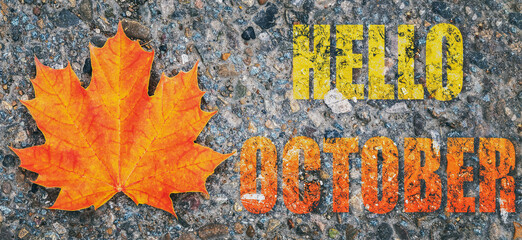 an autumn maple orange leaf lies on the asphalt with the inscription hello October, autumn background, autumn toned image