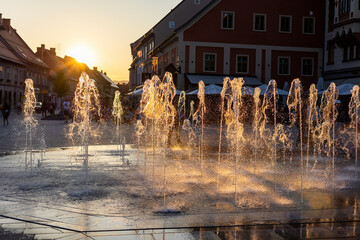 Water spraying from fountain in city of Maribor, Slovenia, at sunset. Splashing droplets from...