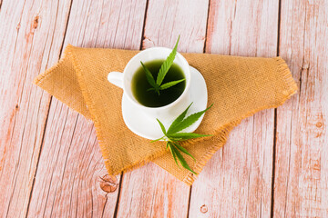 Hot Cannabis herbal tea and marijuana leaves on wooden table.