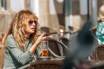 middle-aged woman on terrace sending voice message with mobile phone or smartphone