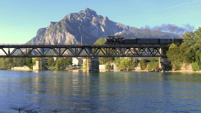 ancient steam locomotive crossing an ancient iron bridge over a river with mountains in the background. steam train