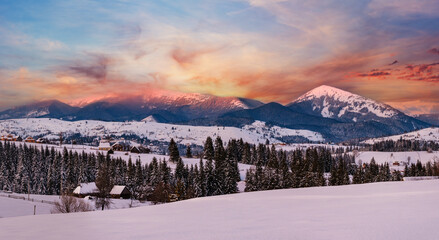 Alpine village outskirts panorama in last evening sunset sun light. Winter snowy hills and fir...