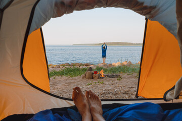 view from a tent on the shore of a lake or sea, a woman collects firewood or does yoga and...
