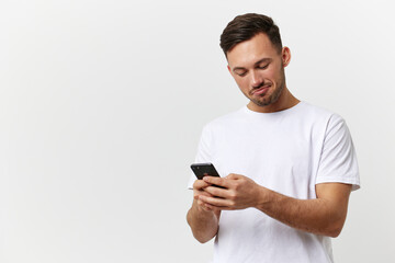 Happy passionate tanned handsome man in basic t-shirt doing online shopping with phone posing isolated on over white studio background. Copy space Banner Mockup. Mobile gaming RPG concept