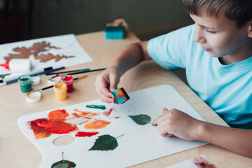 Cute child sitting at desk and making picture from dry birch leaves