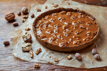 Autumn or winter food. Autumn thanksgiving dessert. Tart with caramel and walnut on baking paper on wooden table