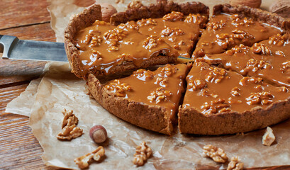 Closeup of slice of tart with caramel and walnut. Baking paper on wooden table. Autumn or winter treats. Autumn thanksgiving dessert.