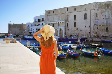 Holidays in Apulia, Italy. Back view of beautiful fashion girl enjoying view of Monopoli ancient port in Apulia, Italy. Summer vacation in Europe.