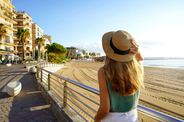 Tourism in Calabria. Back view of girl holding straw hat walking on Crotone promenade on Calabria...