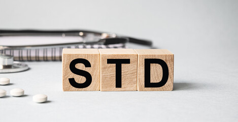 STD inscription on wooden cubes isolated on white background, medicine concept. Nearby on the table are a stethoscope and pills.