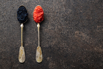 Red and black caviar in silver spoons on dark table.
