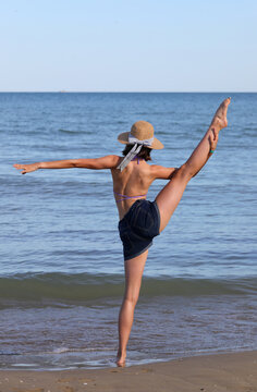 young slender girl in straw hat does gymnastic exercises by the sea